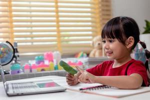 Learning time. Interested little kid schoolgirl in headset sit at home desk watch education video lesson. Curious small school age girl think on teacher question select correct answer on laptop screen photo