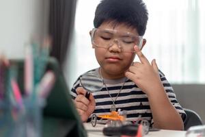 Young asia student remotely learn online at home  in coding robot car and electronic board cable in STEM, STEAM, mathematics engineer science technology computer code in robotics for kids. photo