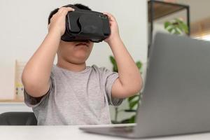 niño asiático con anteojos vr estudiando ciencias en casa, estudiante curioso usa un auricular de realidad virtual para estudiar ciencia en casa estudio en línea aprendizaje de estilo de vida futurista foto