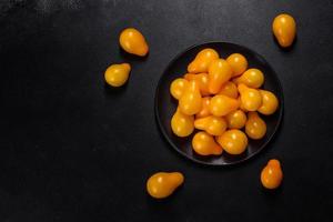 pequeños tomates amarillos en forma de pera en un plato de cerámica sobre una mesa de hormigón oscuro foto