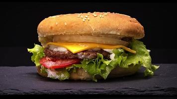 close-up vista de hambúrguer frito suculento com queijo cheddar girando sobre um fundo escuro. conceito de comida deliciosa. cheeseburger, natural sem maquiagem. video