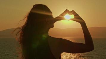 mujer haciendo corazón con sus manos. silueta de brazos femeninos que muestran el símbolo del amor con la puesta de sol en el interior. video