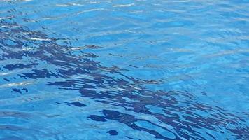 El material de archivo de fondo de la superficie del agua presenta un primer plano extremo del agua azul en una piscina. el agua se ondula en cámara lenta y tiene algunos reflejos del sol. video