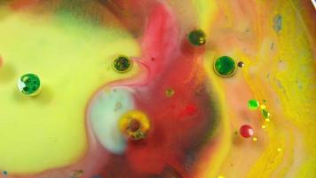 Colorful abstract bubbles and drops are flowing on the yellow and red water surface as macro video