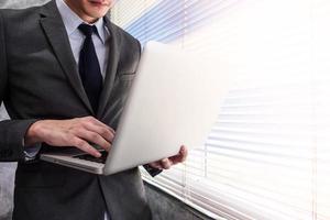 Close up of businessman using laptop while standing at a window in an office photo