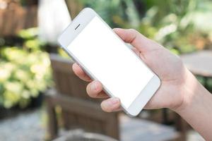 mujer sosteniendo un teléfono inteligente de pantalla vacía en la mano con fondo verde de primavera foto