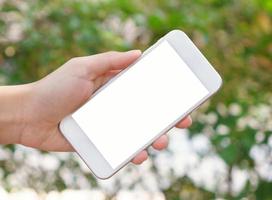 mujer sosteniendo un teléfono inteligente de pantalla vacía en la mano con fondo verde de primavera foto