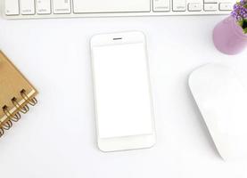 vista superior del teléfono inteligente de pantalla en blanco en el trabajo de mesa blanca foto