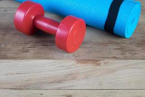 Blue yoga mat and Red dumbbell on wood background photo