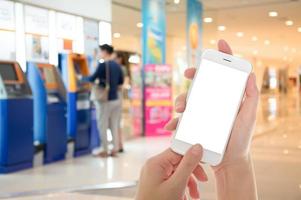 Woman hand showing smart phone with isolated screens display with Background of People Using ATM as Mobile Banking Concept photo