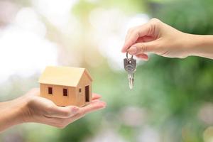 mano de mujer sosteniendo una casa modelo y una llave, comprando un nuevo concepto de casa foto