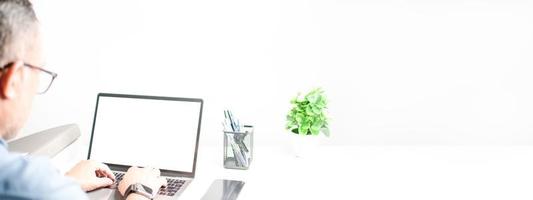 Men typing on a keyboard to use computer network. Laptop blank, white screen. Concept work at home with computers and Internet. Notebook computer on a white table. Copy space on right, blur background photo