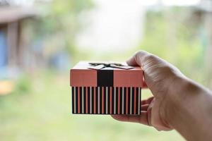 The one hand holding a present box with background blurred and copy space on top. The image is a closeup and is landscape. photo