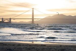 Golden Gate Bridge at dusk with a gold brown pastel sky and an outline of a kite surfer photo