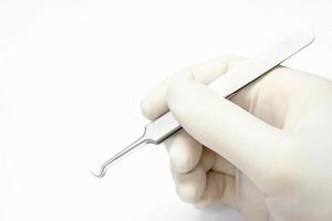 Hand of doctor in a white medical latex glove holding a blackhead forceps remover and showing the gesture of holding the forceps isolate on white background and make with photo