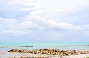 Rock mound on the beach with beautiful green sea under the light blue sky. photo