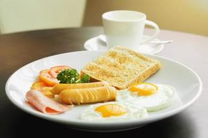 desayuno americano y café caliente en una taza de café de cerámica blanca sobre una mesa de madera con el cálido sol de la mañana. foto