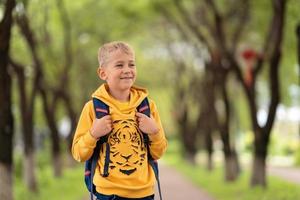 un chico rubio con una sudadera amarilla y una mochila sobre los hombros yendo a la escuela foto