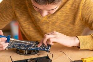 a young man solders a burnt-out microcircuit with a soldering iron photo