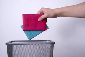 A hand throws two passports into a trash garbage can against a gray background. photo