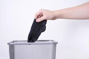 A man is throwing an old sock into a trash can with his hand against a white background. photo