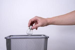 A hand throws a light bulb into a trash can against a gray background. photo