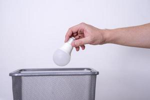 A hand throws a light bulb into a trash can against a gray background. photo