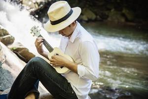 Man play ukulele new to the waterfall - people and music instrument life style in nature concept