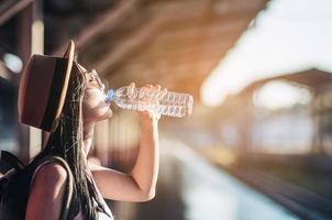 Young woman back pack traveler drink fresh water in train station - outdoor asian traveler activity concept