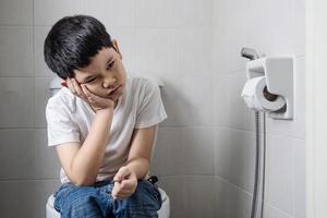 Asian boy sitting on toilet bowl holding tissue paper  - health problem concept photo