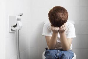 Asian boy sitting on toilet bowl holding tissue paper  - health problem concept photo