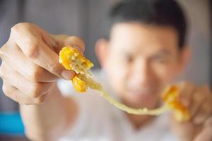 Man is going to eat sticky stretch fried cheese ball. Photo is focused at cheese ball