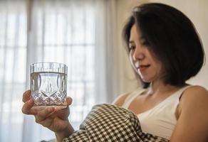 Asian woman drink water after wake up in the morning sitting on a bed - health care concept photo