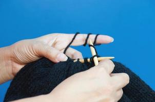 Woman's hands is making black hat knitting over light blue background photo