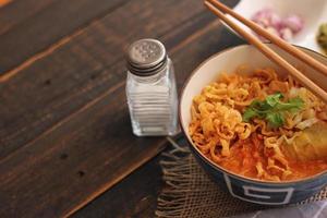 comida tailandesa, sopa de fideos al curry al estilo norteño servida en un tazón estampado de estilo artístico. en la mesa de madera negra foto