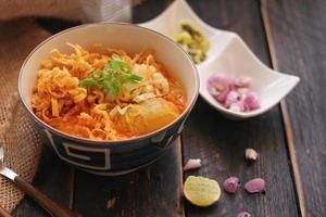 comida tailandesa, sopa de fideos al curry al estilo norteño servida en un tazón estampado de estilo artístico. en la mesa de madera negra foto