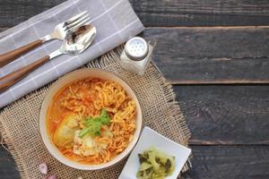 comida tailandesa, sopa de fideos al curry al estilo del norte servida en un tazón estampado de estilo artístico. en la mesa de madera negra foto