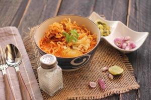 comida tailandesa, sopa de fideos al curry al estilo norteño servida en un tazón estampado de estilo artístico. en la mesa de madera negra foto