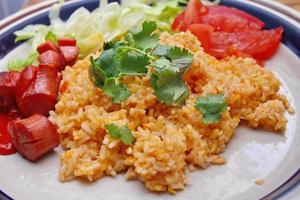 Fried rice with fried sausage served in a creamy dish with tomatoes and cucumbers. photo