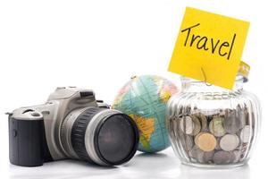 monedas en botella de vidrio con cámara y globo sobre fondo blanco, ahorrando dinero para viajar foto
