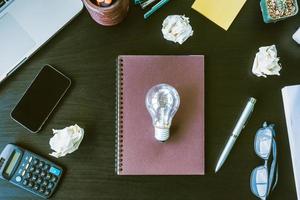 Top view notebook with crumpled paper balls and light bulb on the desk. photo