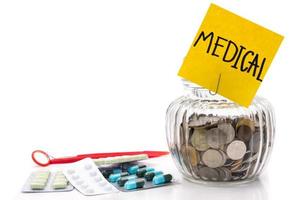 monedas en botella de vidrio con medicina sobre fondo blanco, ahorrando dinero para gastos médicos foto