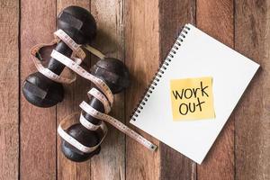 Top view of iron dumbbells with measure tape and notebook on wooden table background. photo