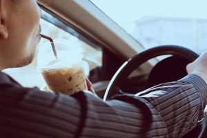 Man is dangerously drinking cup of cold coffee while driving a car photo