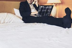 Business man using telephone while working on his computer in hotel room during travel photo