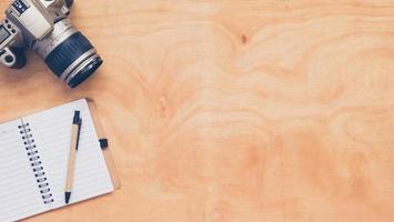 Top view of camera with notebook and pen on wooden table background. photo