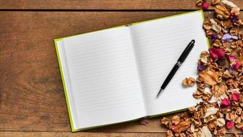 Top view workspace with blank notebook,pen and dried flowers on wooden table background . photo