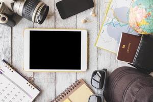 Top view of Tablet with camera,calendar,smart phone,earphones,sunglasses,cap,notebook,wallet,passport,map and globe on white wooden table background, Travel concept photo