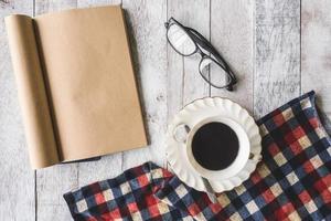 Top view of Coffee cup with tablecloth, notebook and glasses on wooden table background photo