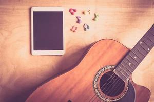 vista superior de la guitarra acústica con el dispositivo de la computadora táctil de la tableta en el fondo de la mesa de madera. imagen de estilo de efecto vintage foto